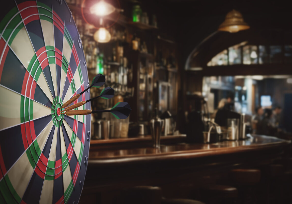 Dart board with three darts outdoors white blured bar background.