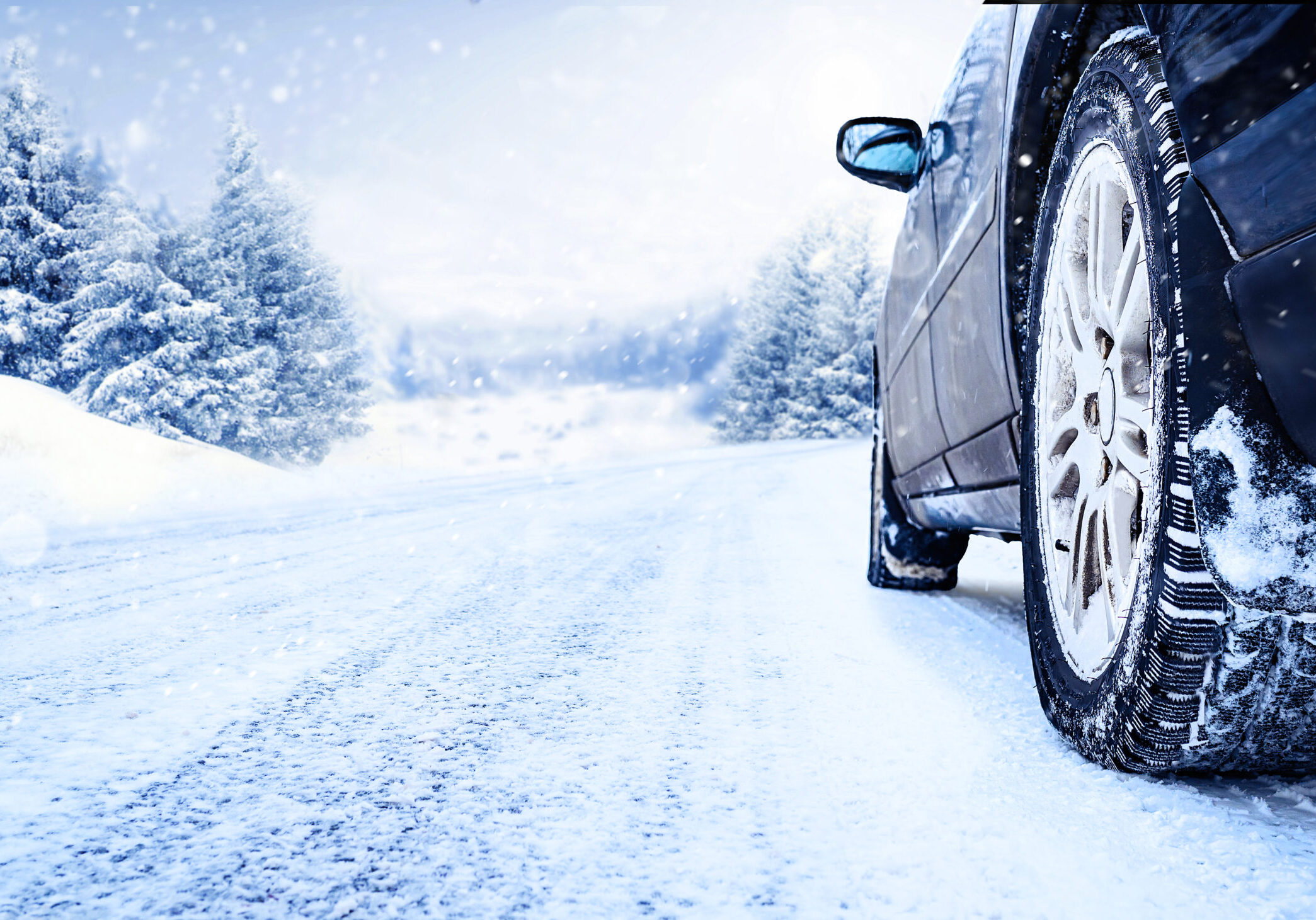 Winter tire closeup. Car on snowy road with beautiful landscape.