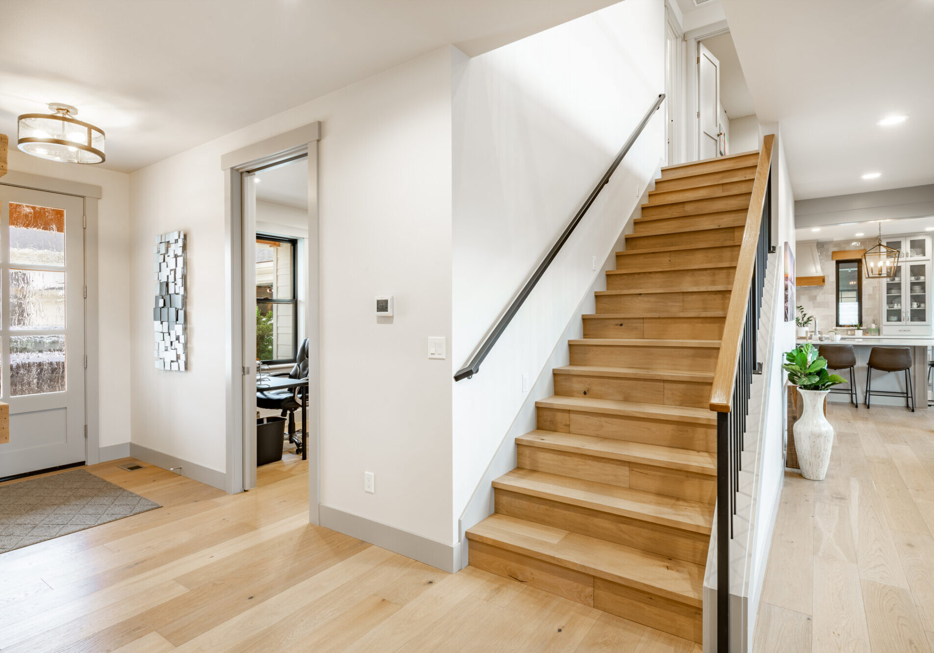 Beautiful home painted white with a modern farmhouse vibe. Entrance foyer to a lovely home with hardwood floors large staircase with wrought iron metal railings, post and beam entry. Decorated with simple furniture and a very welcome feeling.