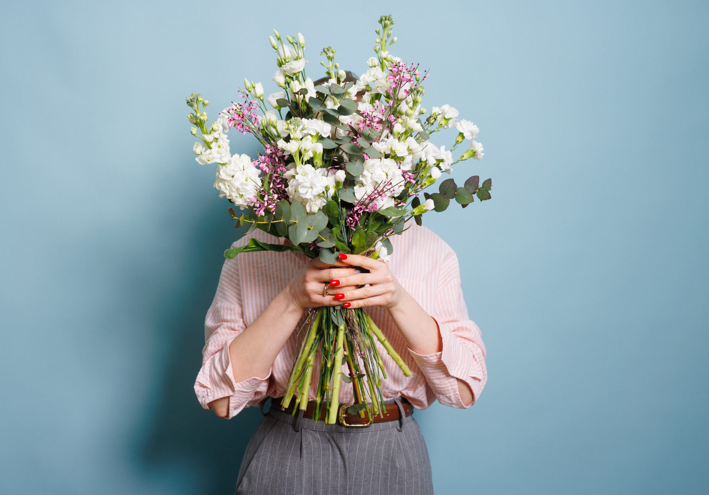 girl covers her face with a bouquet of flowers on a clean blue background