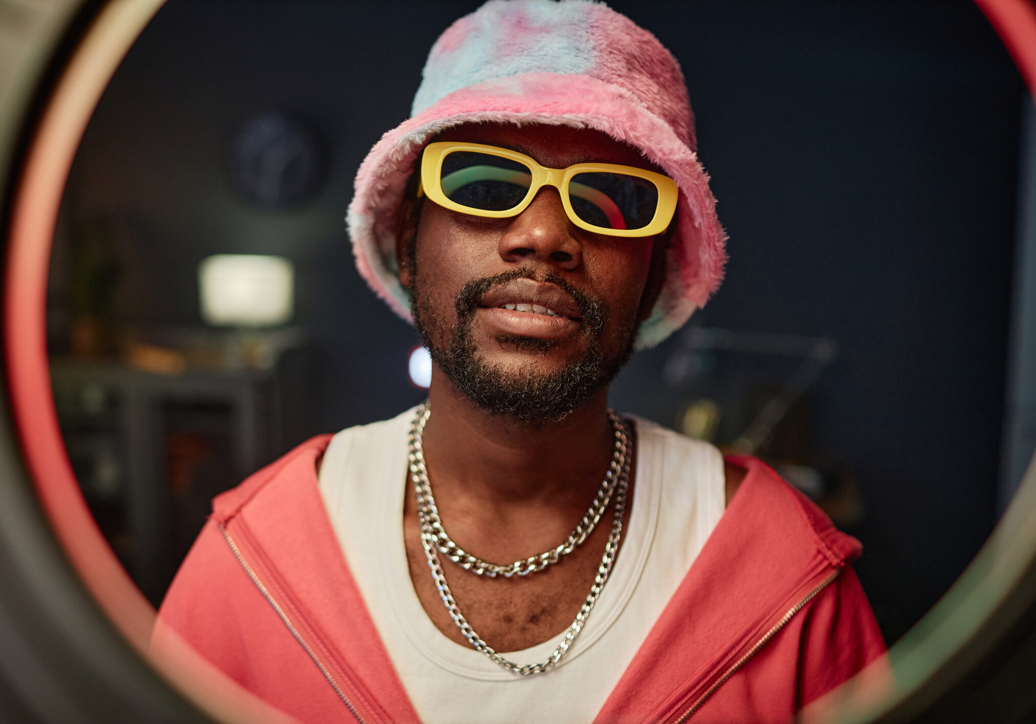 Front view portrait of trendy African American man wearing pink outfit recording videos for social media through ring light