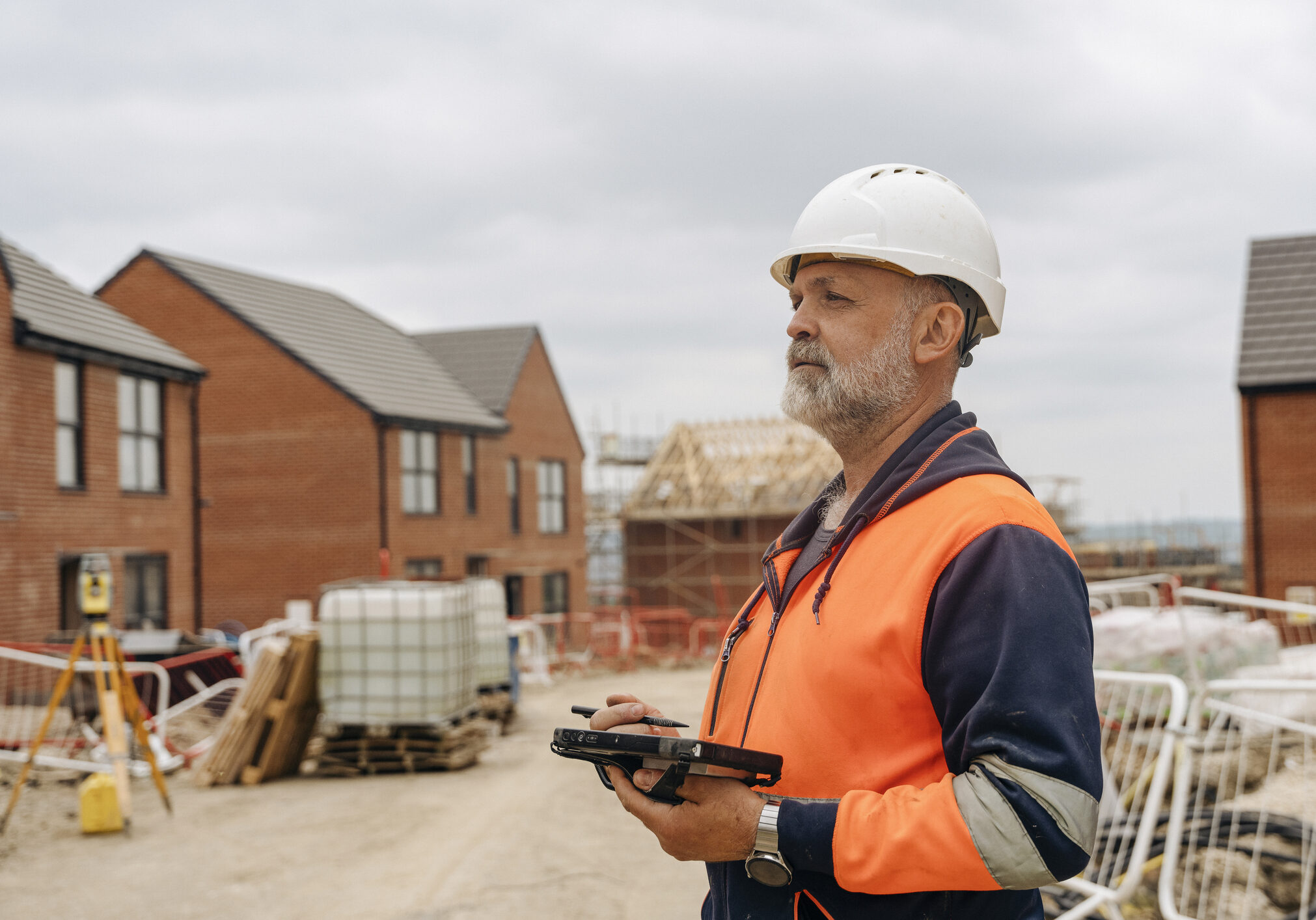 Construction Worker Using Tablet Controller Computer To Operate EDM Total Station at New Home Development