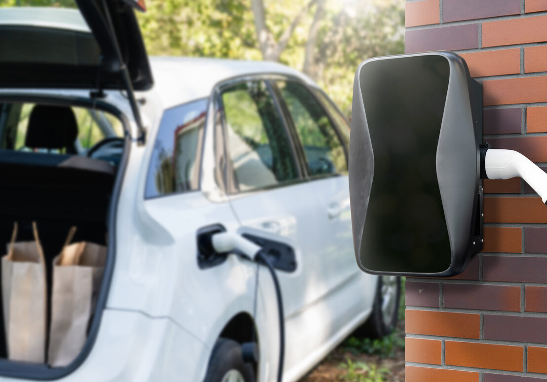 Charging electric car next to house with charging station on the wall.