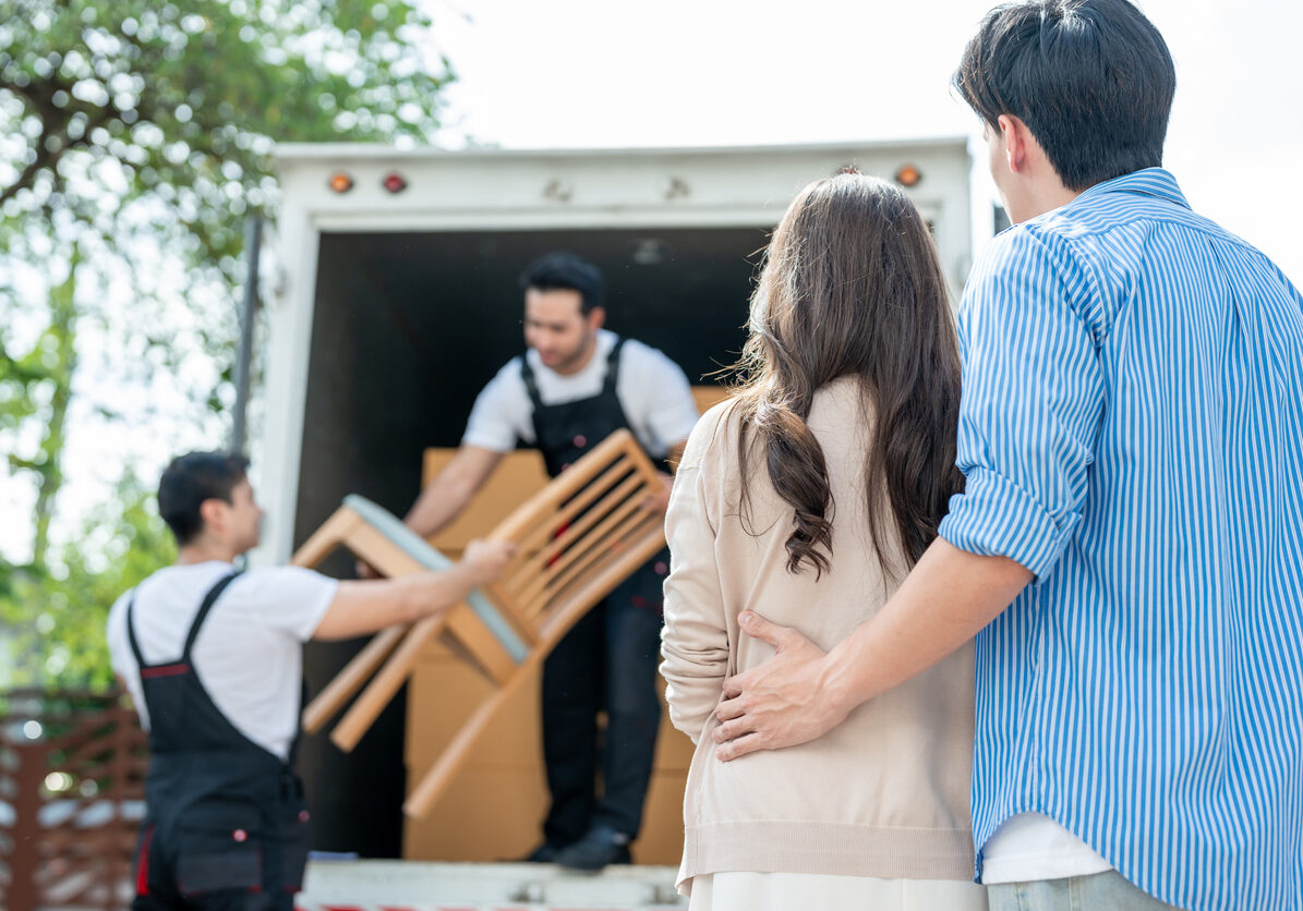 Caucasian delivery man worker delivering package to young couple in house. Attractive courier employee working and deliver box cardboard from car truck infront of new house of new marriage partner.