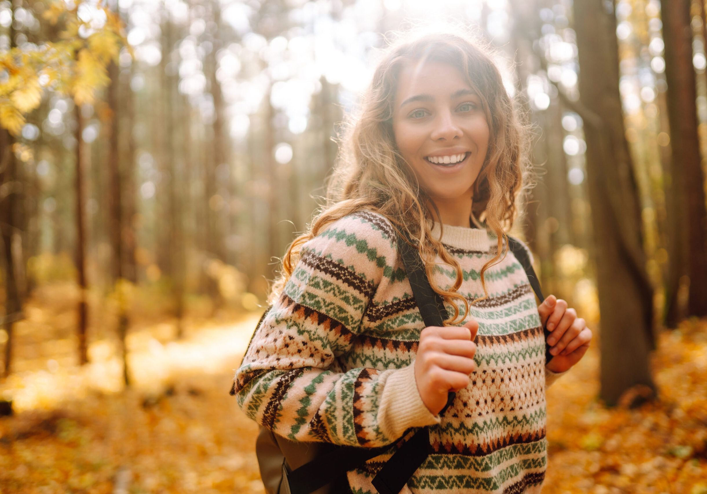 Woman enjoying a joyful moment in a sunny autumn forest surrounded by colorful leaves and towering trees