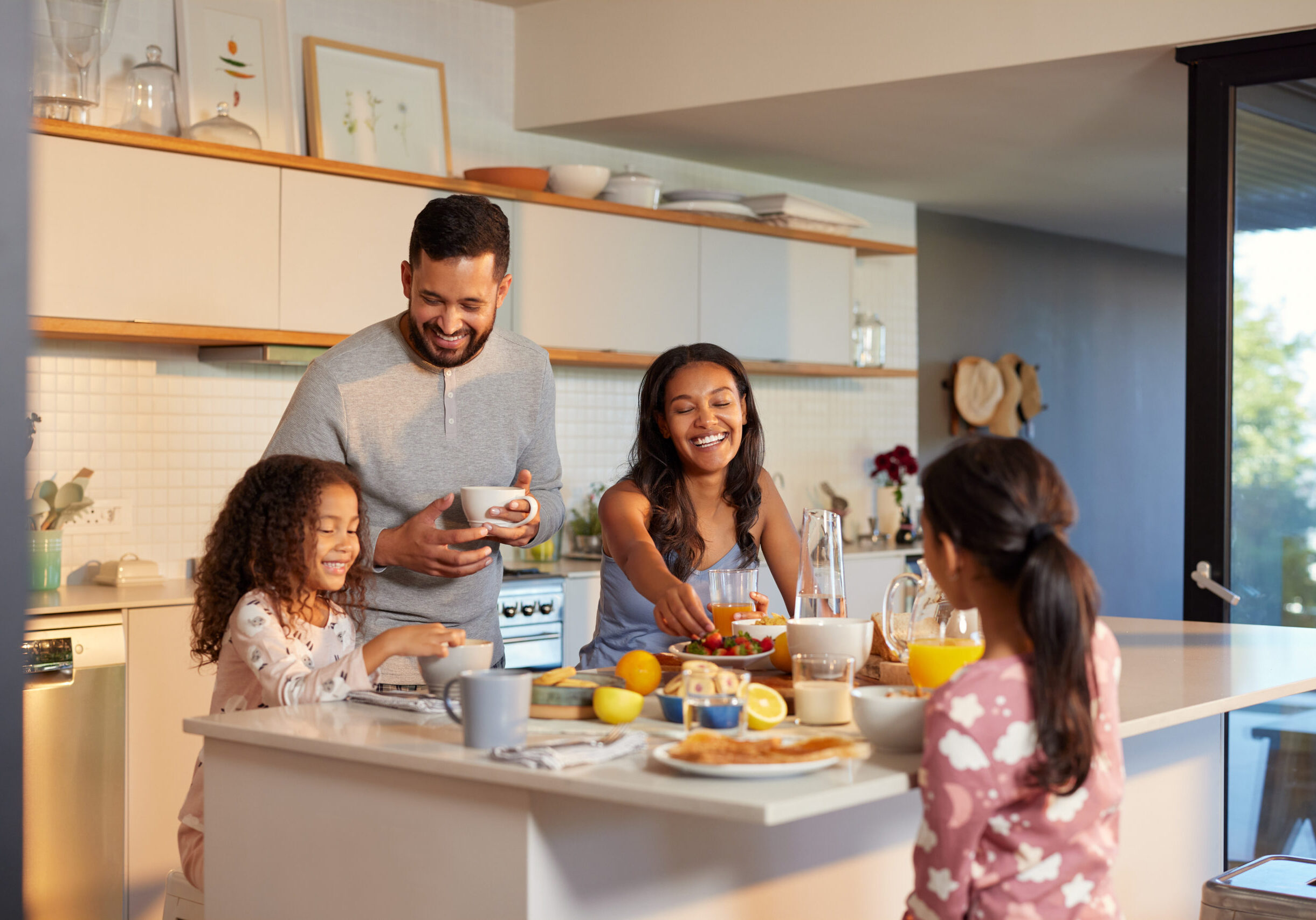 Hispanic parents and smiling little daughters enjoying a cheerful breakfast together in the kitchen. Mixed race mother and father sharing a joyful morning meal around the kitchen island with their cute little girls. Multiethnic family starting their day with healthy meal in their cozy home.