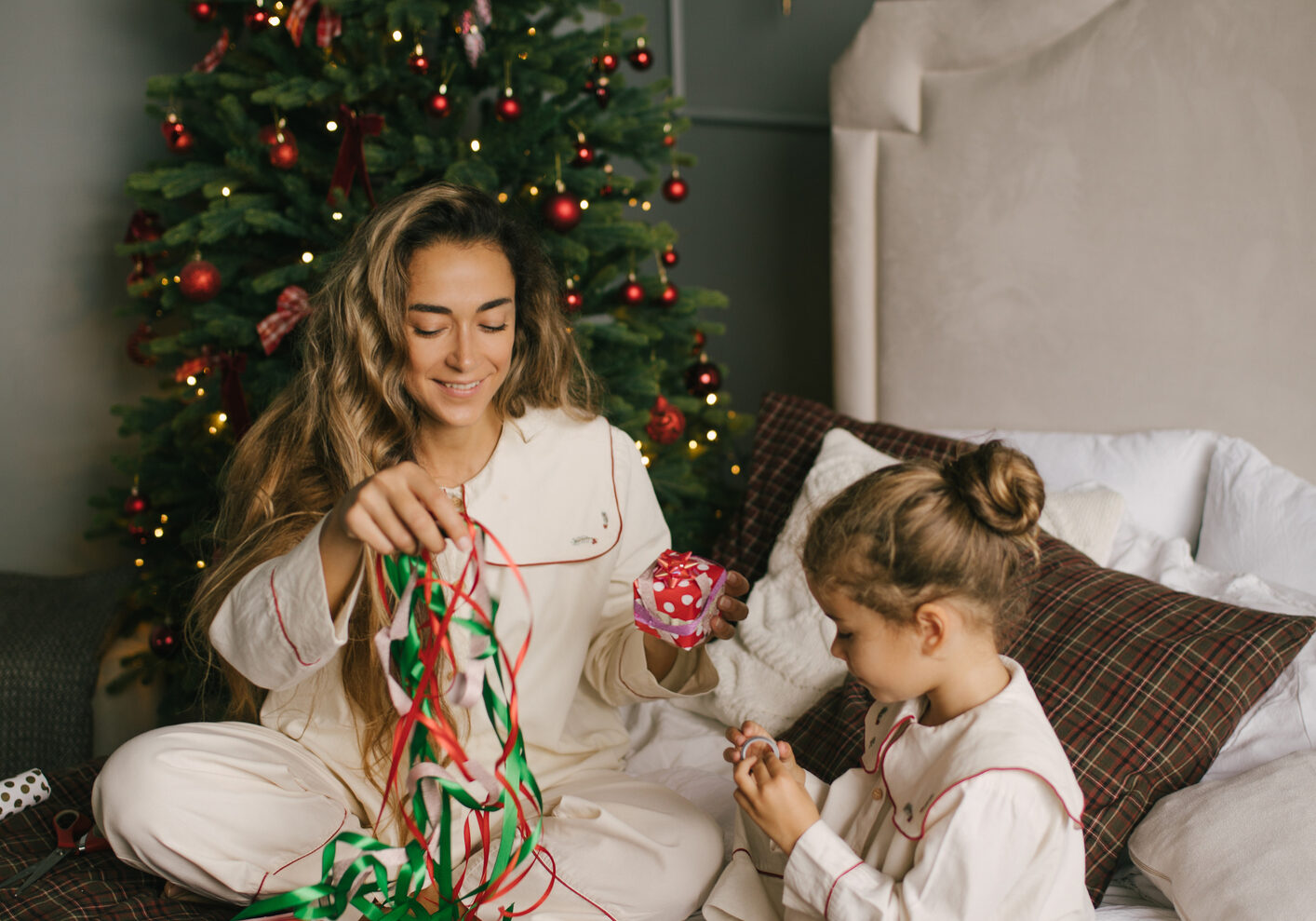 mother and daughter packing and wrapping presents in a cosy, decorated bedroom with a Christmas tree.