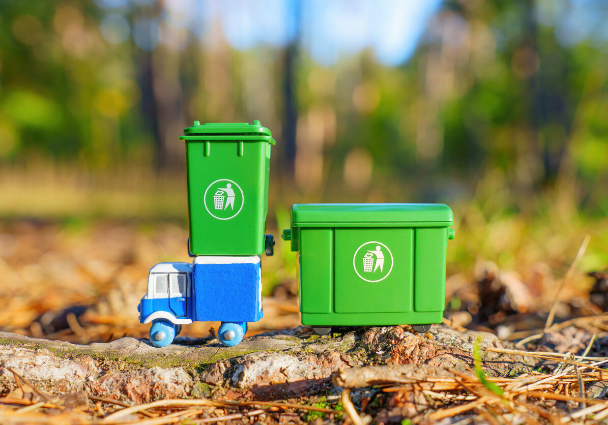 Miniature garbage truck with green recycling bins on forest floor.