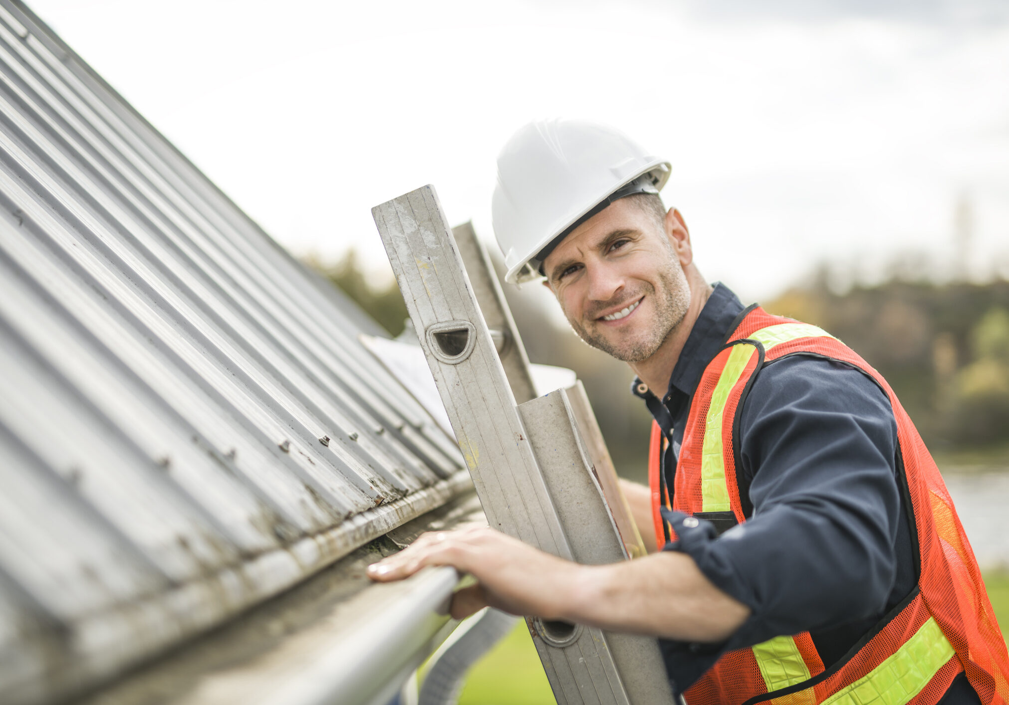 A man with hard hat standing on steps inspecting house roof