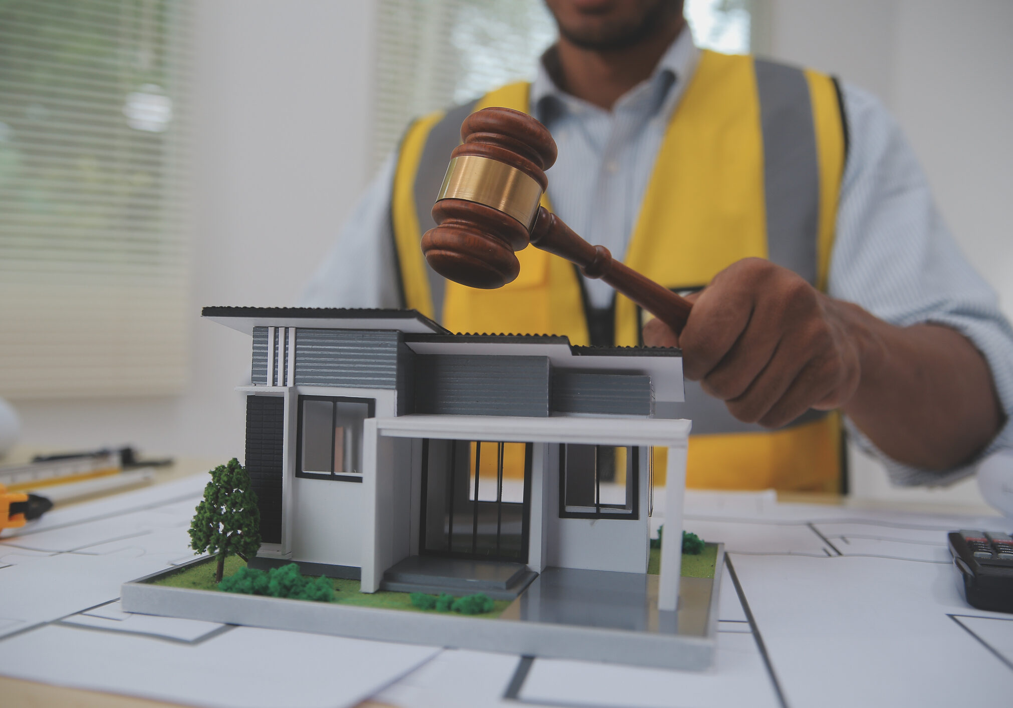 Judge gavel on building blueprint plans with a yellow safety helmet in the background. law that deals with matters relating to building construction, engineering. Construction law concept.