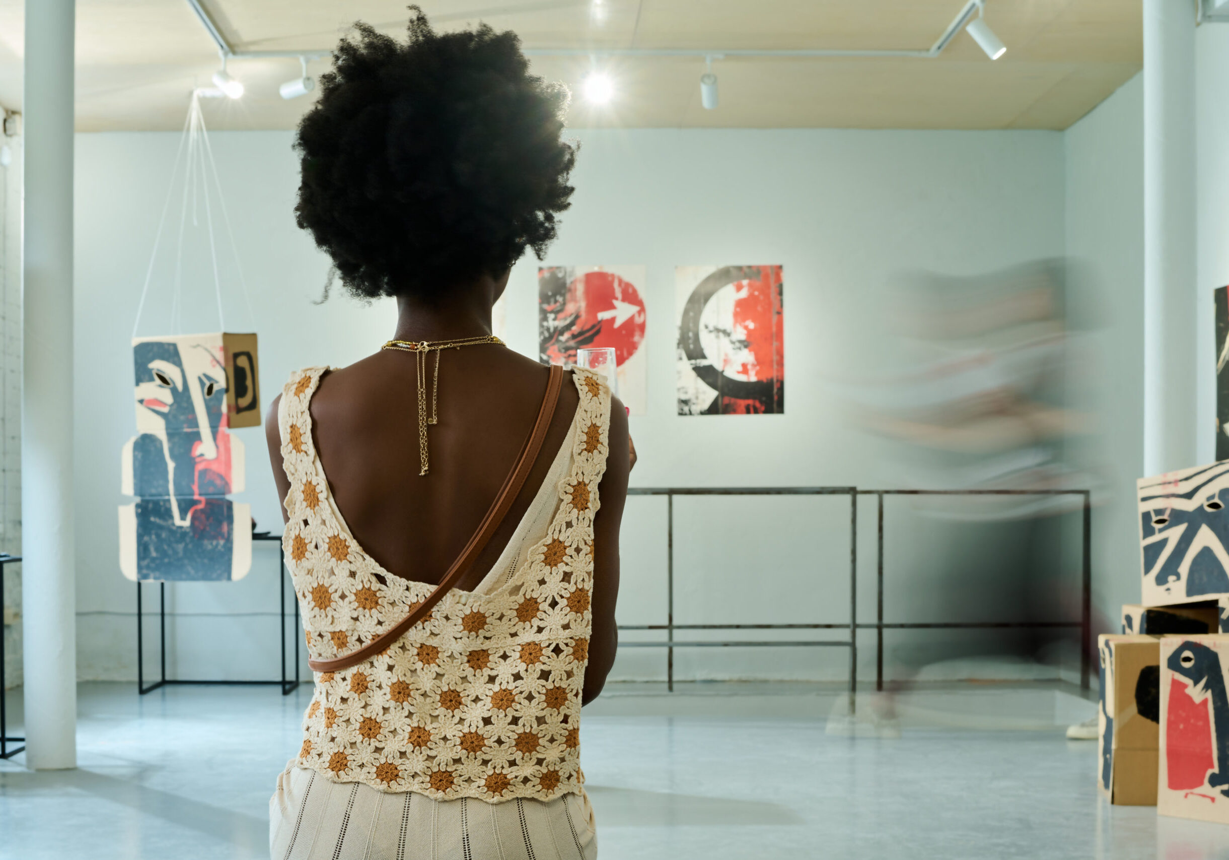Back of young African American female visitor of vernissage wearing elegant apparel standing in spacious gallery hall