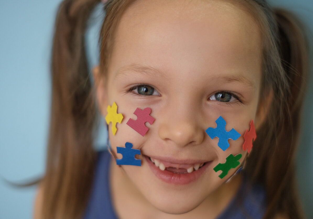 Close-up of a laughing child's face with puzzles pasted on his cheeks. The concept of autism
