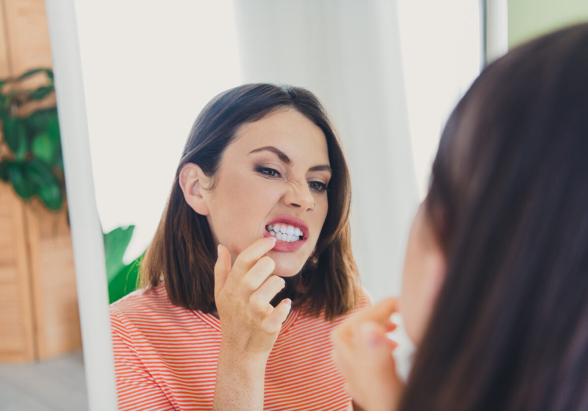Young woman examining her teeth in mirror with a playful expression at home