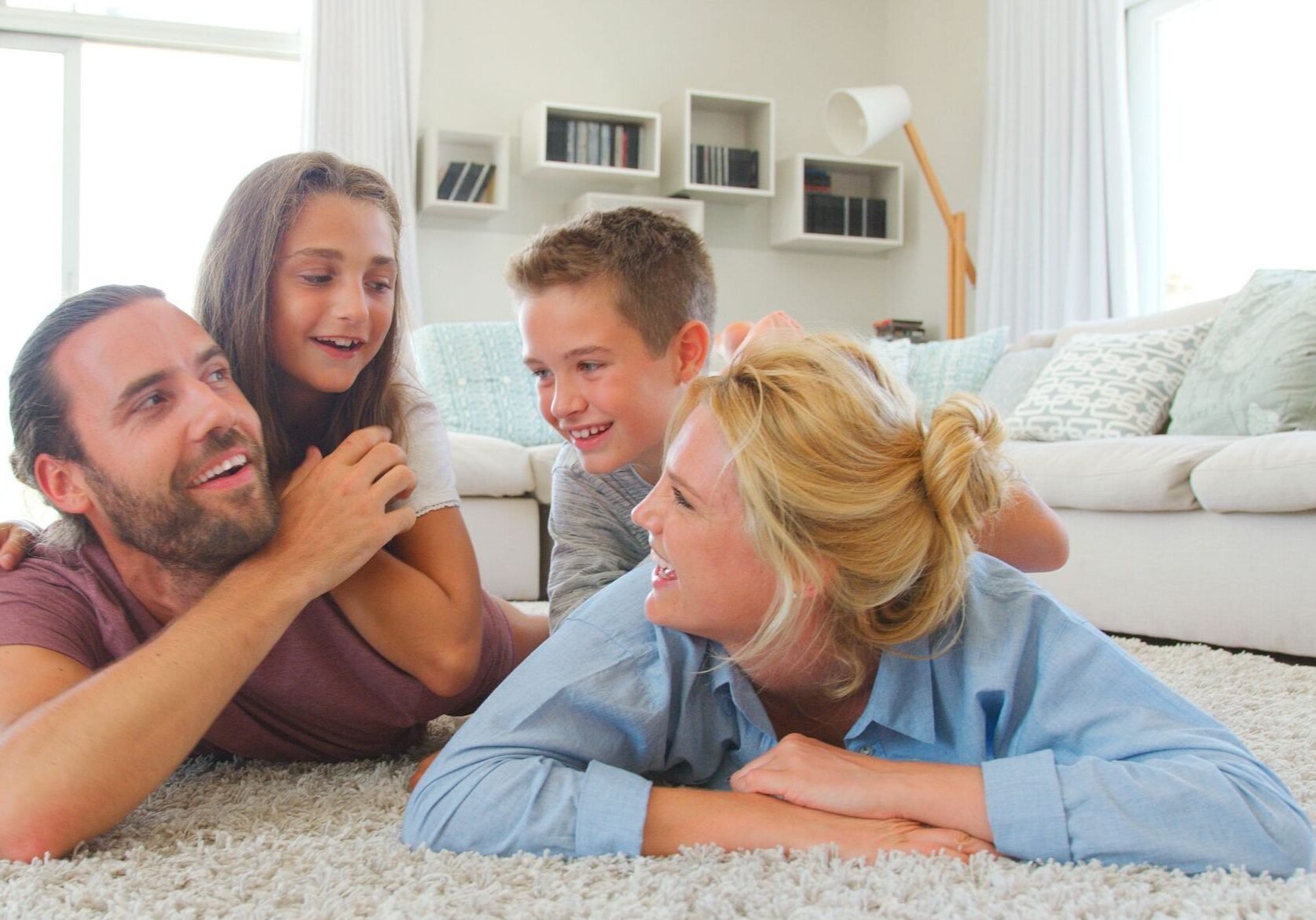 Laughing Children Lying On Parents Backs On Rug In Lounge At Home