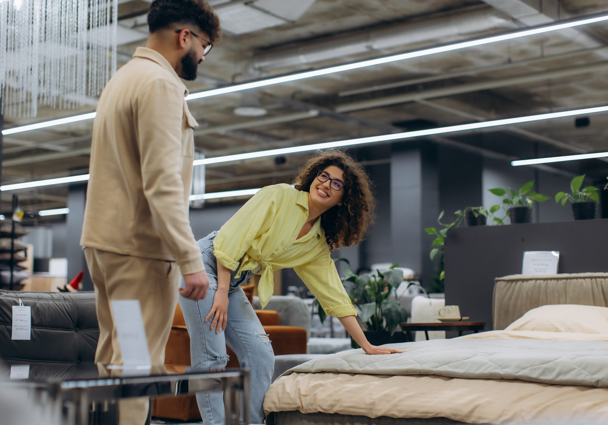 Young couple shopping for a new bed, evaluating a mattress in a modern furniture showroom. Buying home furnishings