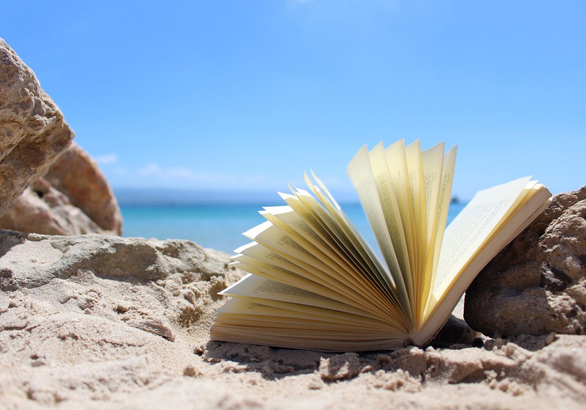 Photo of an open book left on the sand in the windy beach on the coast of Sardinia, Italy, Europe