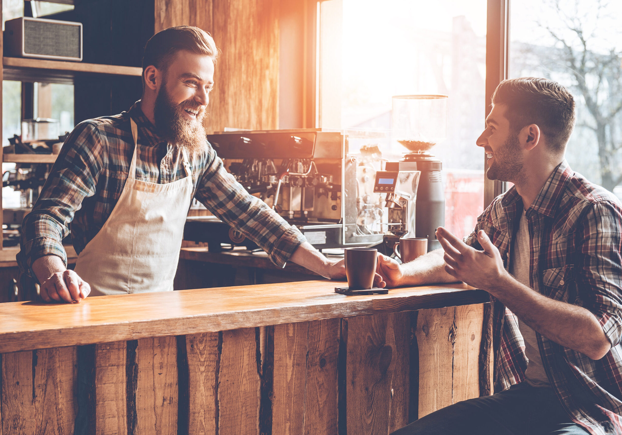 Barista and his customer discussing something with smile while sitting at bar counter at cafe