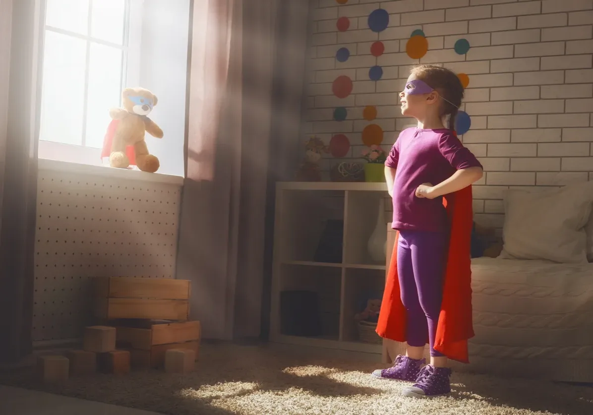 Little child girl plays superhero. Child plays with her friend a Teddy bear. Girl power concept.
