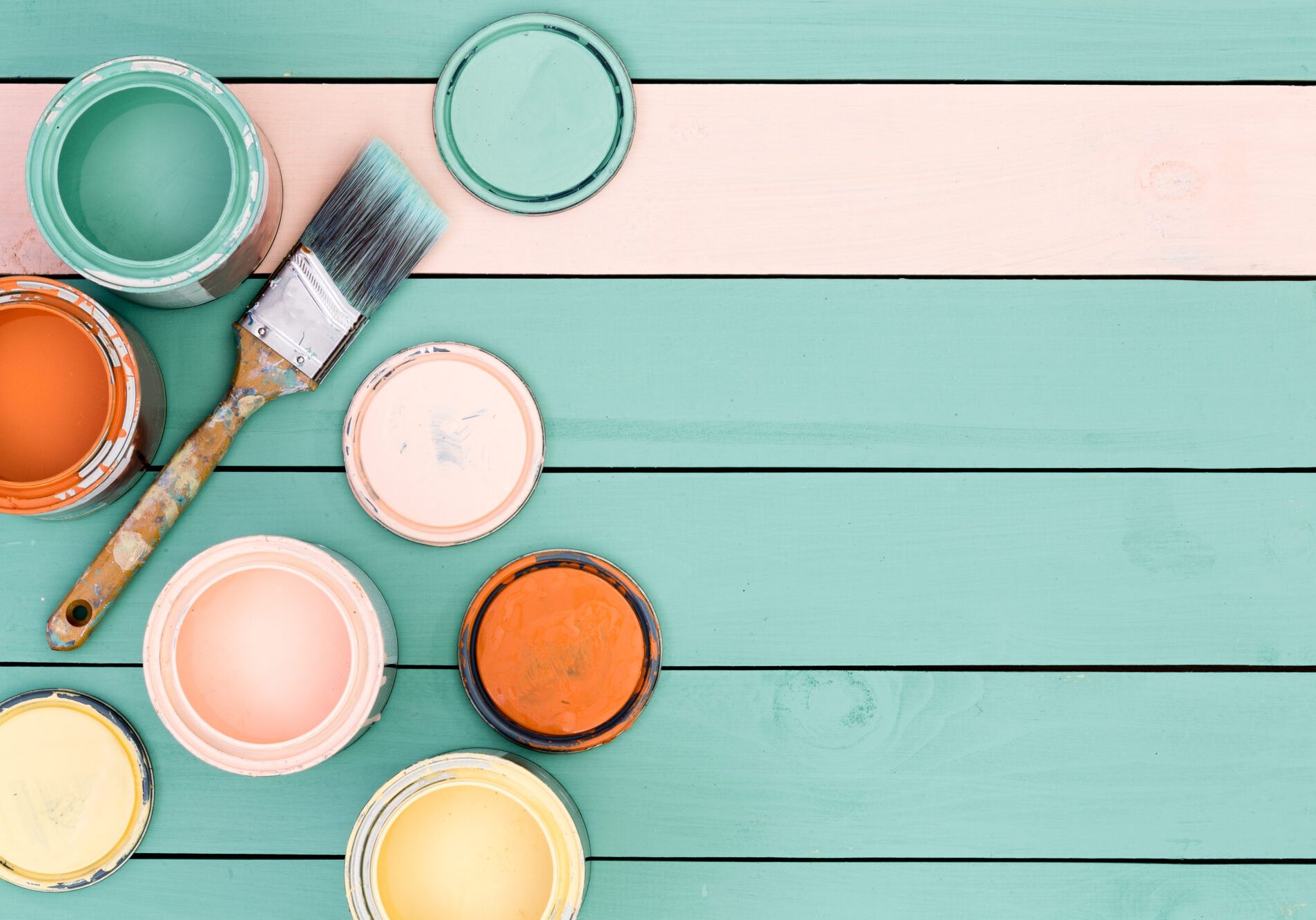 Renovation theme background of floor boards or wooden fence under yellow, pink, orange and green paint cans and brush with copy space
