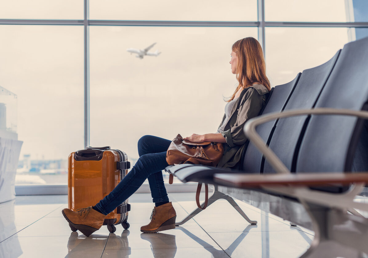 Start of her journey. Beautiful young woman looking out window at flying airplane while waiting boarding on aircraft in airport lounge