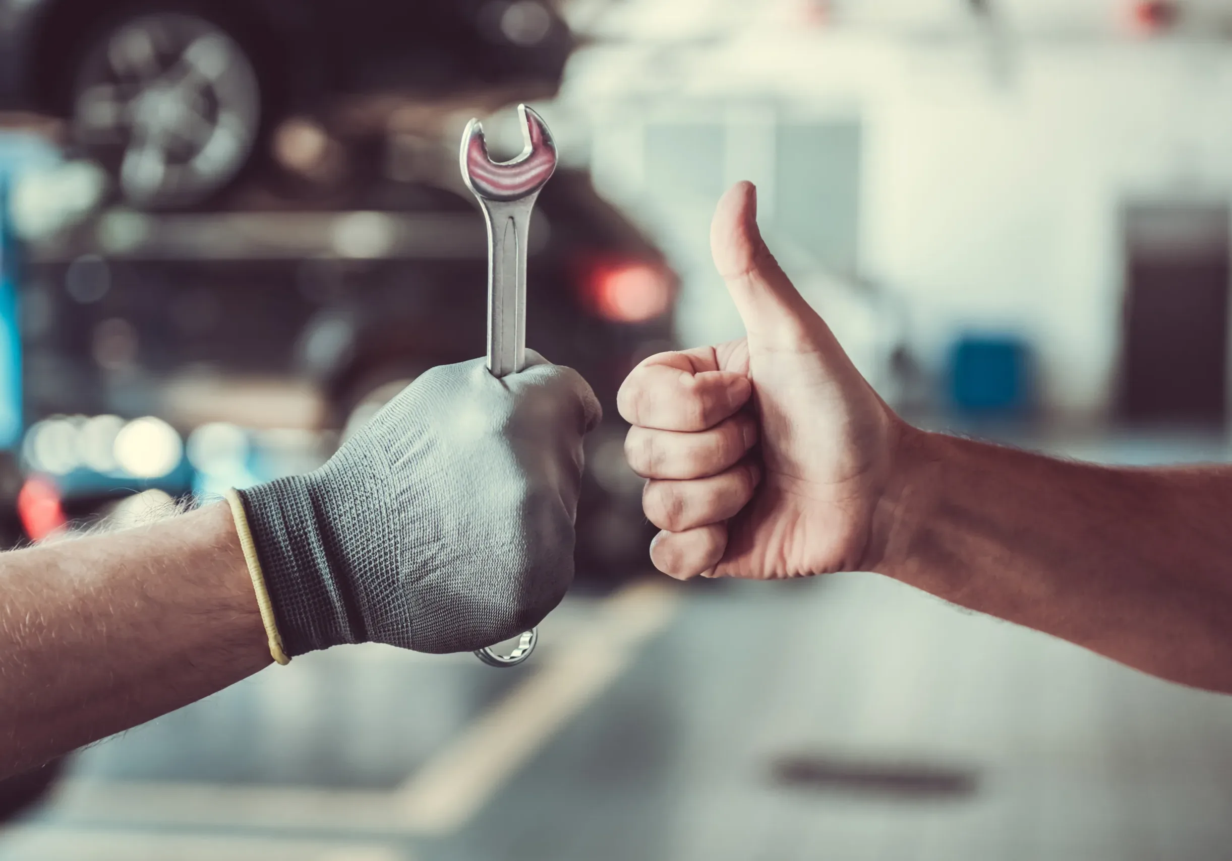 Cropped image of mechanics working in auto service. One is holding a spanner while the other is showing Ok sign