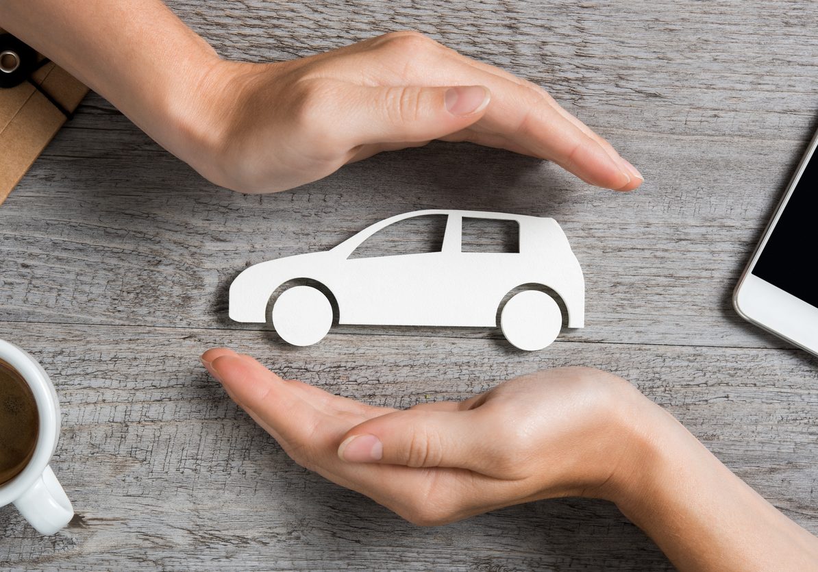 Hands protecting icon of car over wooden table. Top view of hands showing gesture of protecting car. Car insurance and automotive business concept.