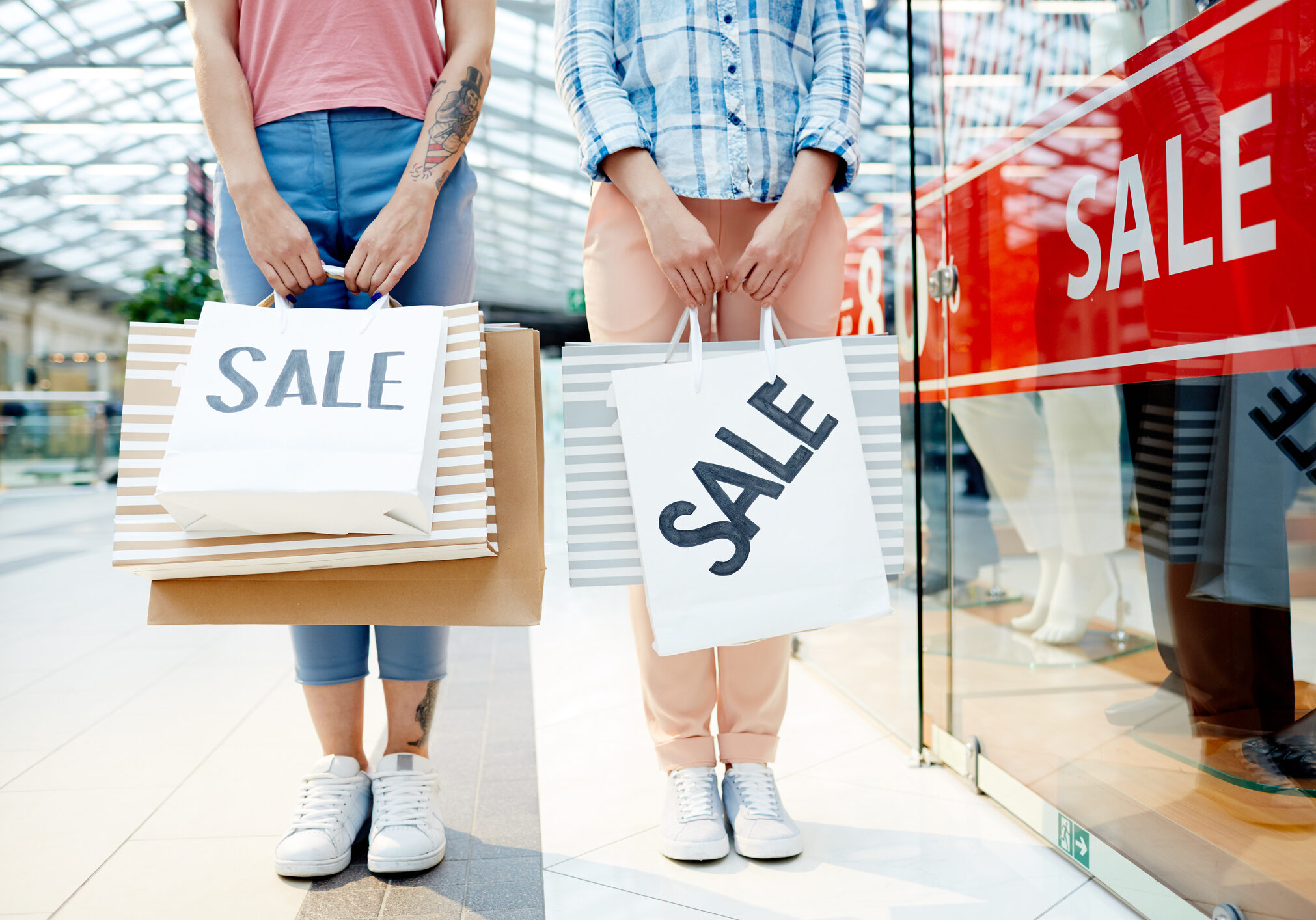 Two friends with paperbags made purchases in mall departments during seasonal sale