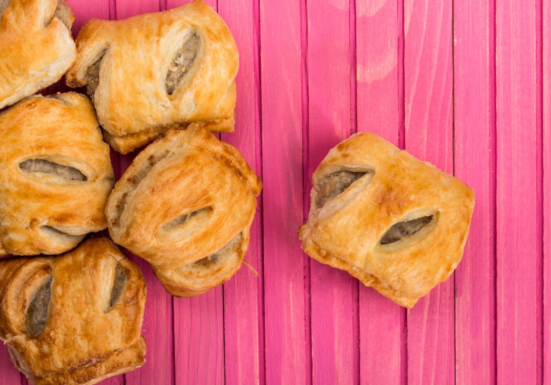 Pile Stack or Selection of Pork Sausage Rolls Savoury Snacks In Pastry On A Pink Wooden Background