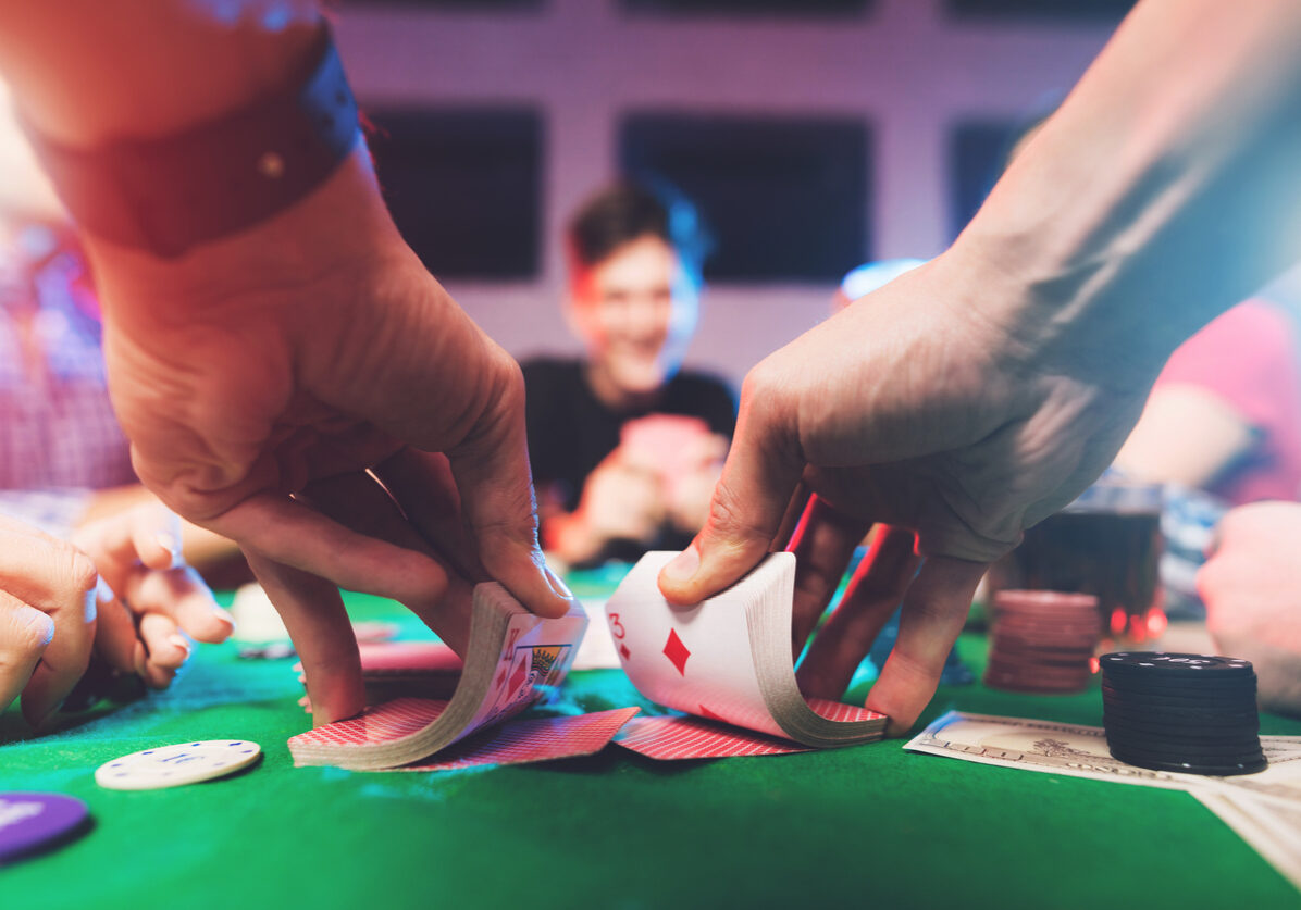 Young people play poker at the table. On the table they have glasses with alcoholic beverages, mobile phones and chips for the game. They have fun playing a game.