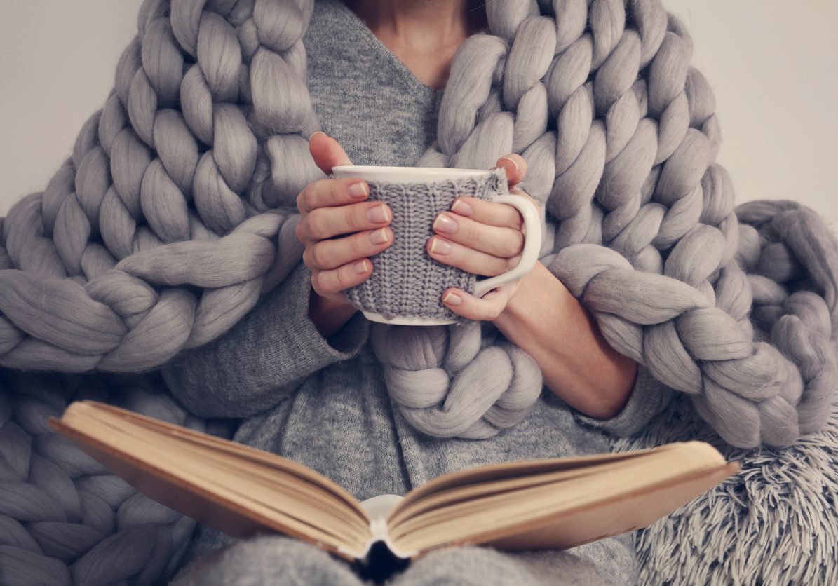 Cozy Woman covered with warm soft merino wool blanket reading a book. Relax, comfort lifestyle.