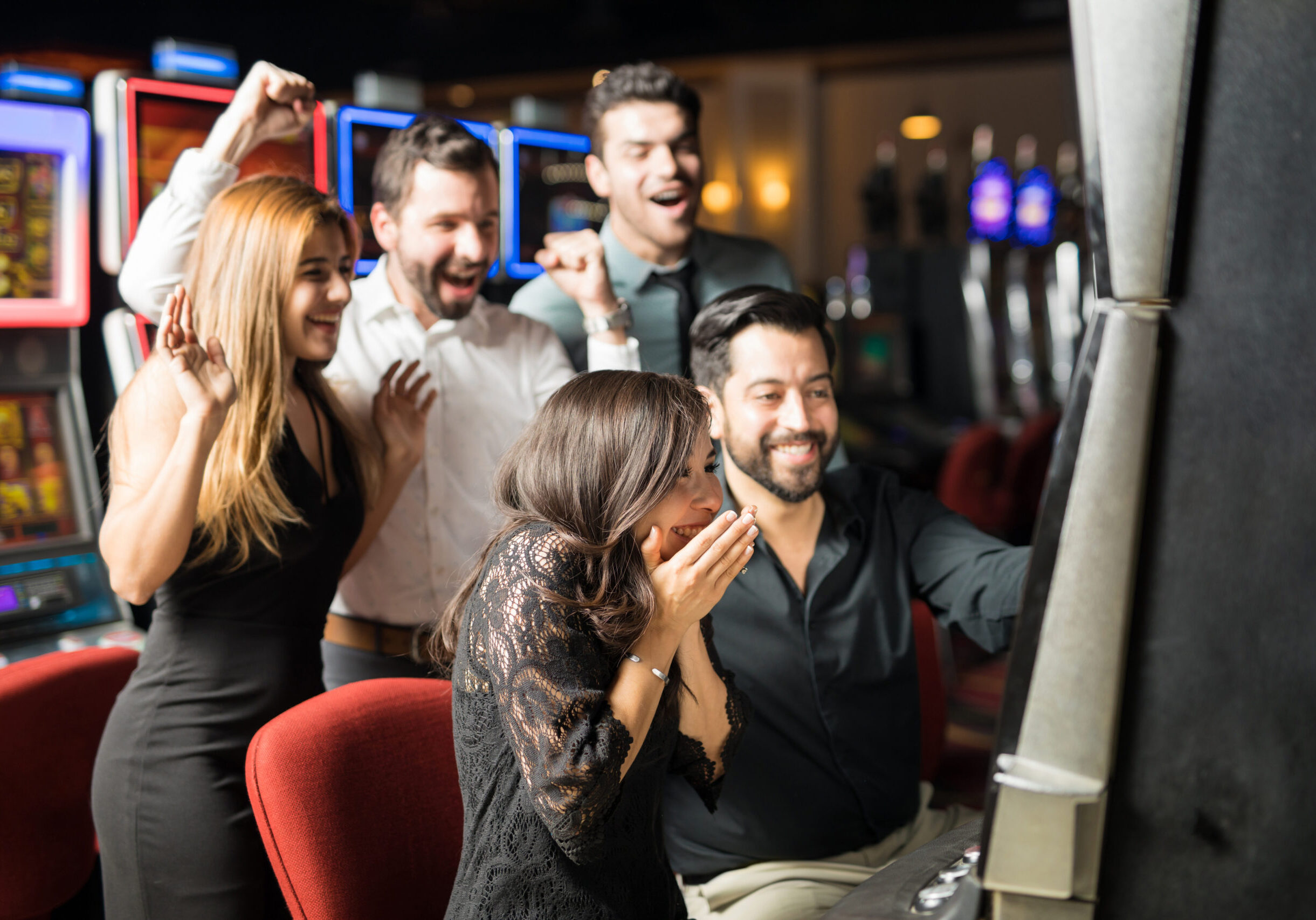 Beautiful Hispanic woman looking excited about hitting the jackpot in a slot machine while her friends celebrate with her