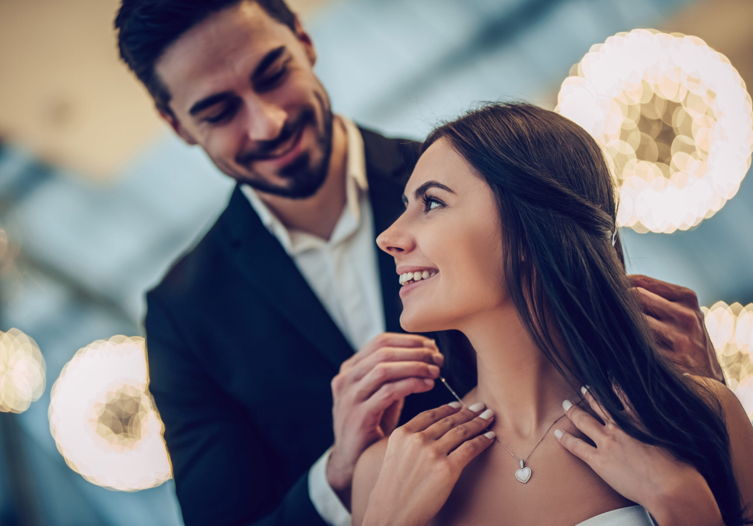 Beautiful loving couple is spending time together in modern restaurant. Attractive young woman in dress and handsome man in suit are having romantic dinner. Celebrating Saint Valentine's Day.