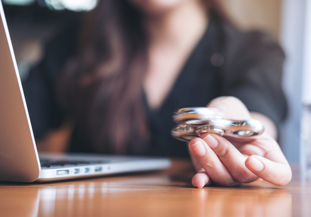 A woman using laptop while playing fidget spinner on wooden table in office