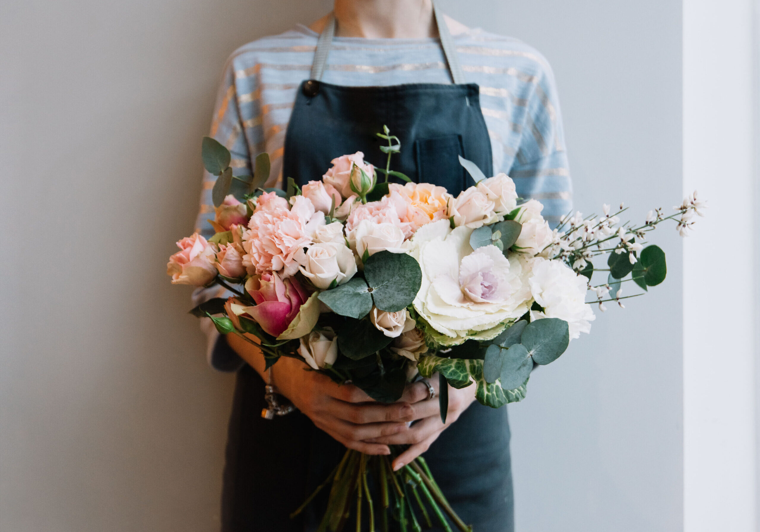 Young florist woman holding freshly made blossoming flower bouquet on the grey wall background.