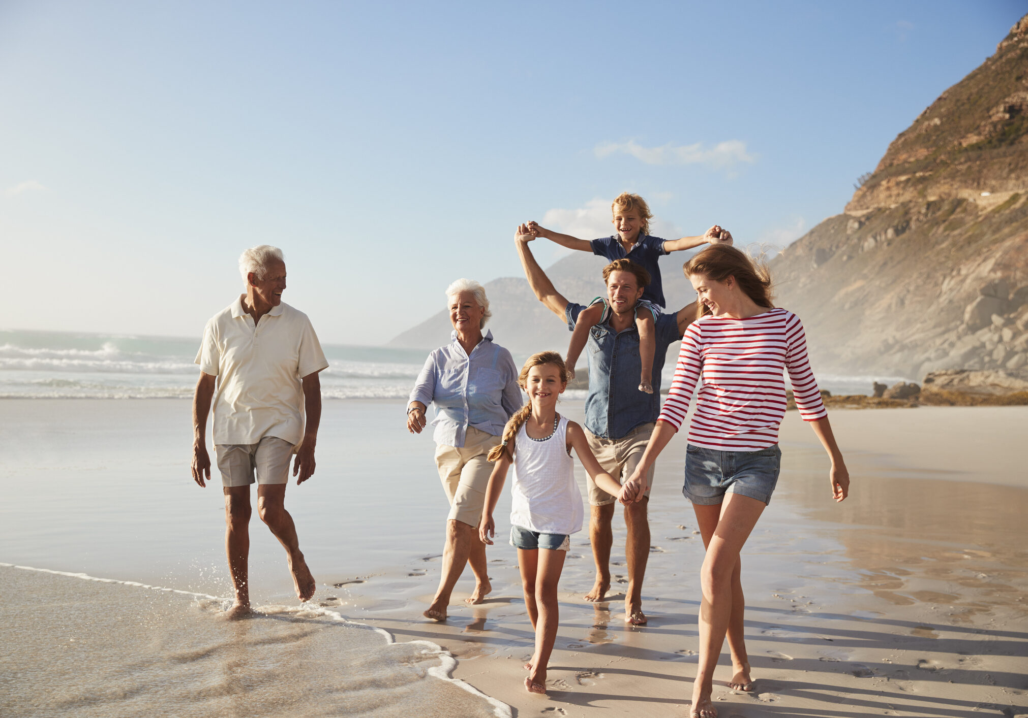 Multi Generation Family On Vacation Walking Along Beach Together