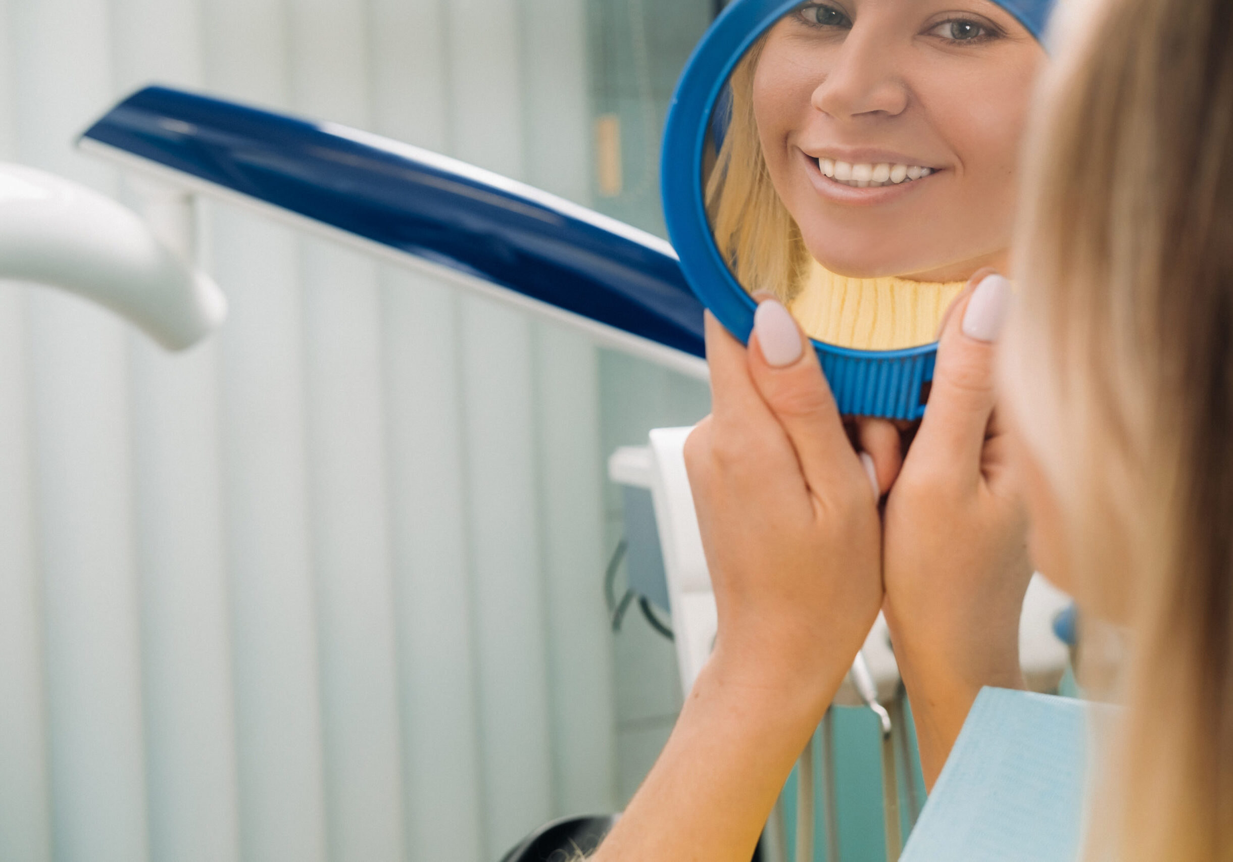 The girl smiles and looks in the mirror in dentistry.